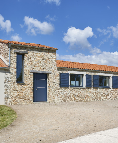 Porte d'entrée aluminium Leucade - Visuel d'ambiance Extérieur maison rénovée en pierre composé d'un ensemble de menuiseries bleues